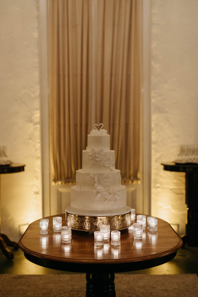 A four tiered wedding cake on a table with small candles around it
