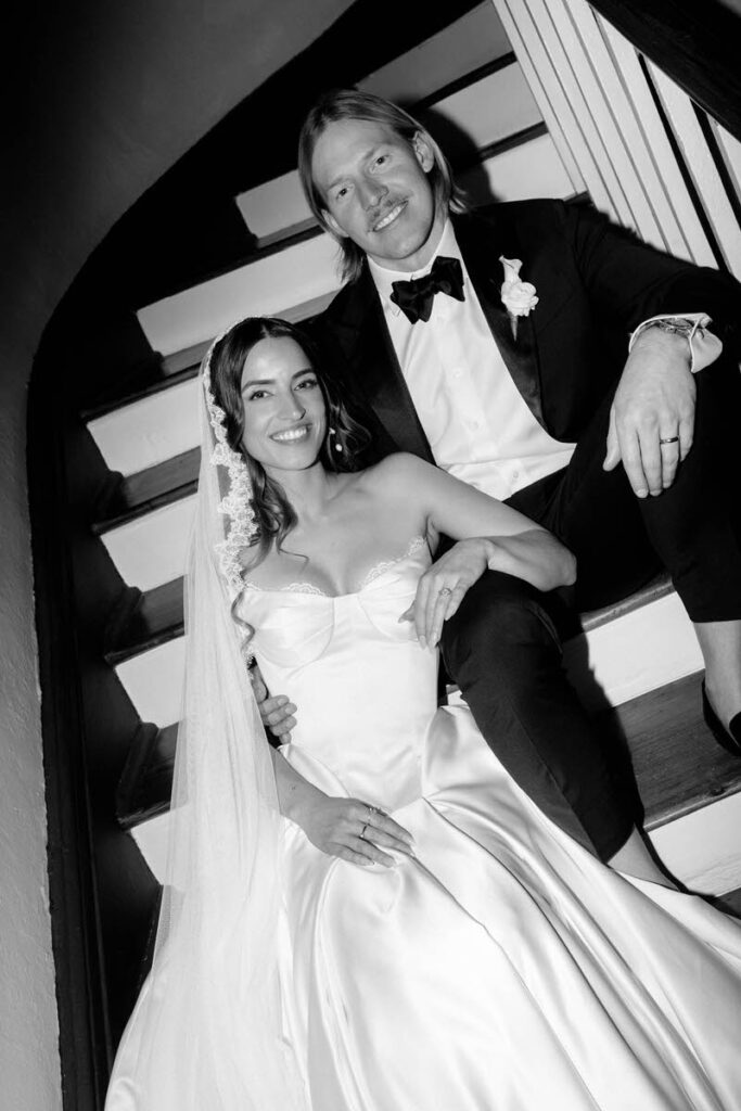 A newlywed couple smiling and sitting on a staircase together