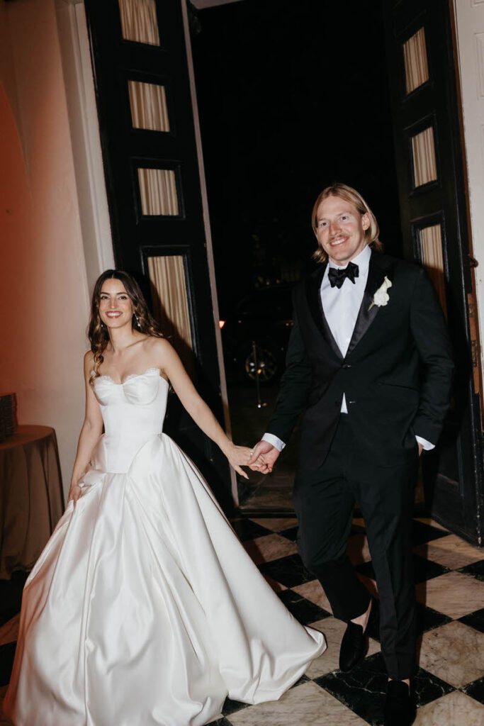 A newlywed couple holding hands and walking into their reception