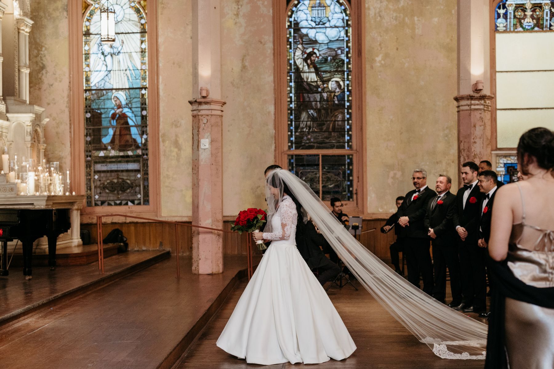 a woman wearing a white wedding dress and veil and holding a bouquet of roses walking down the aisle with her father at hotel peter and paul in new orleans