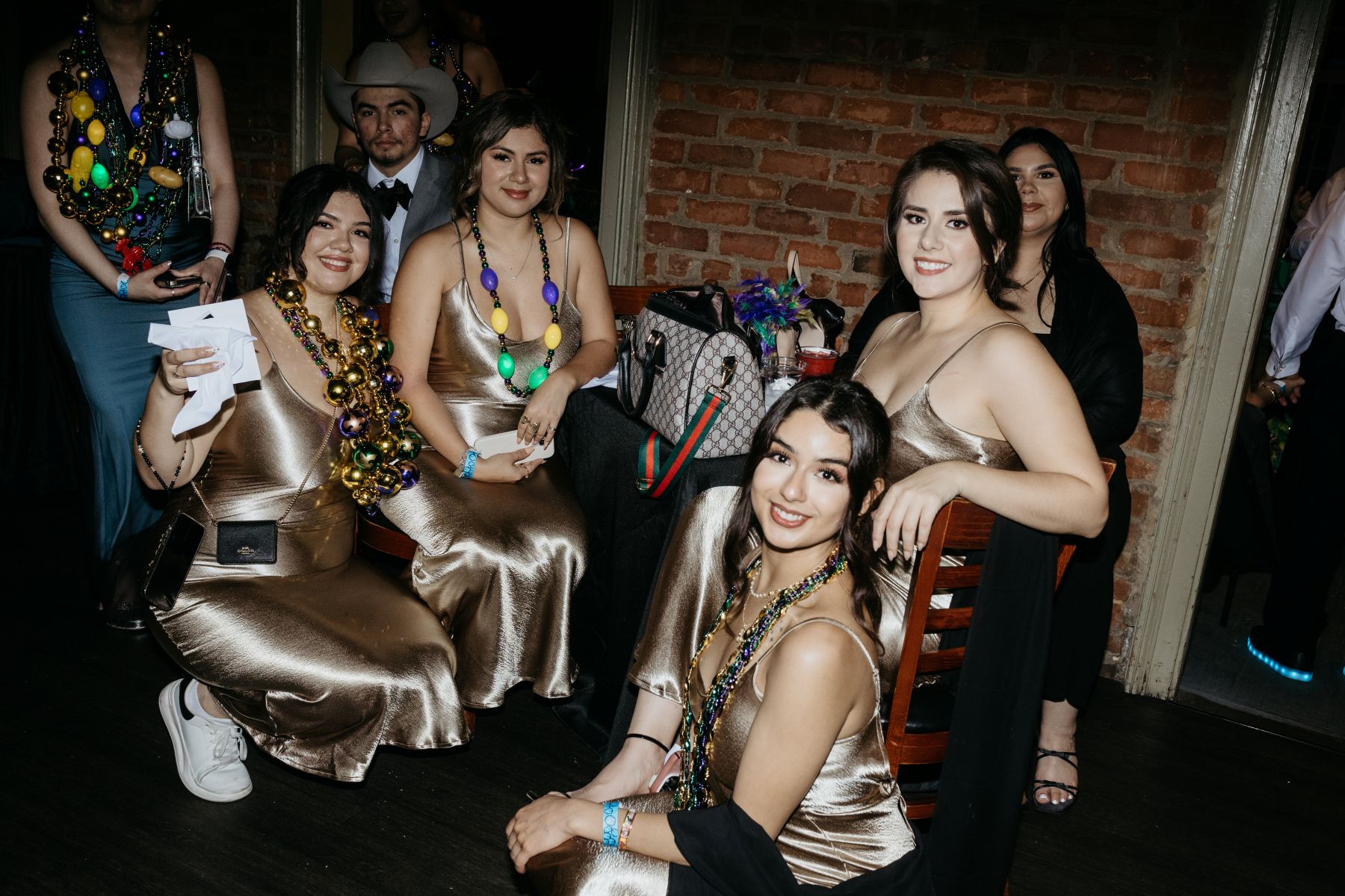 a group of bridesmaids wearing mardi gras necklaces and gold dresses sitting on the balcony at cornet in new orleans 
