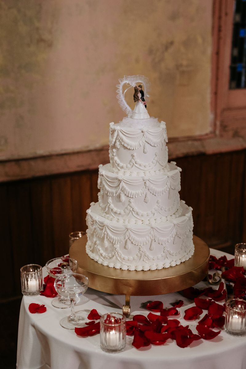 a three tiered white wedding cake on a table with red roses and candles 