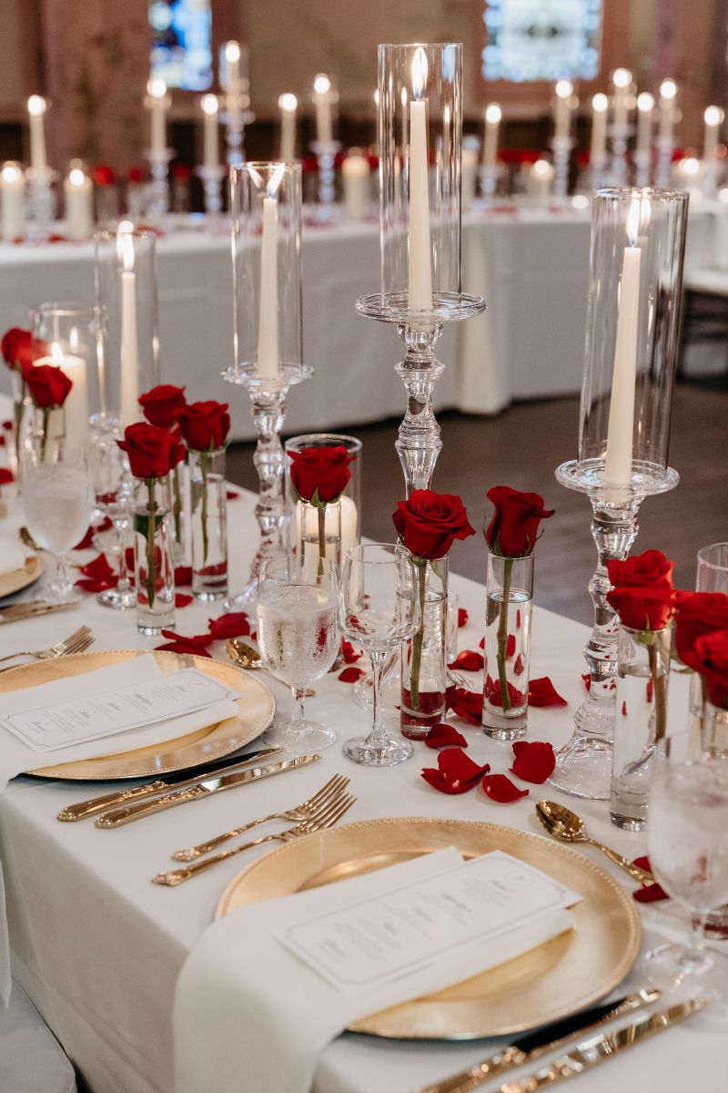 elegant wedding details at a reception in hotel peter and paul including roses in vases, gold plates and cutlery, and candles 