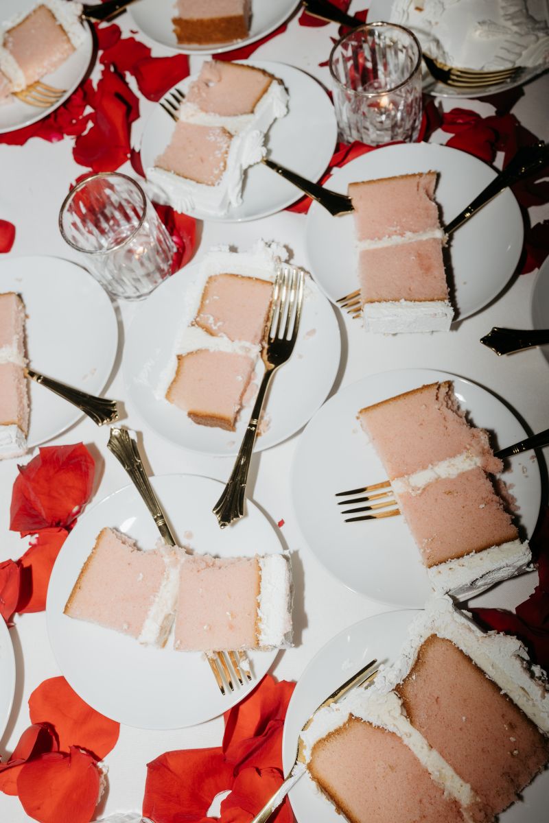 pink wedding cake covered in white frosting on top of table with red rose petals 
