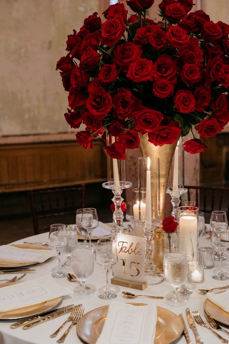 a table decorate with red roses in a gold vase, candles, and gold cutlery and plates 