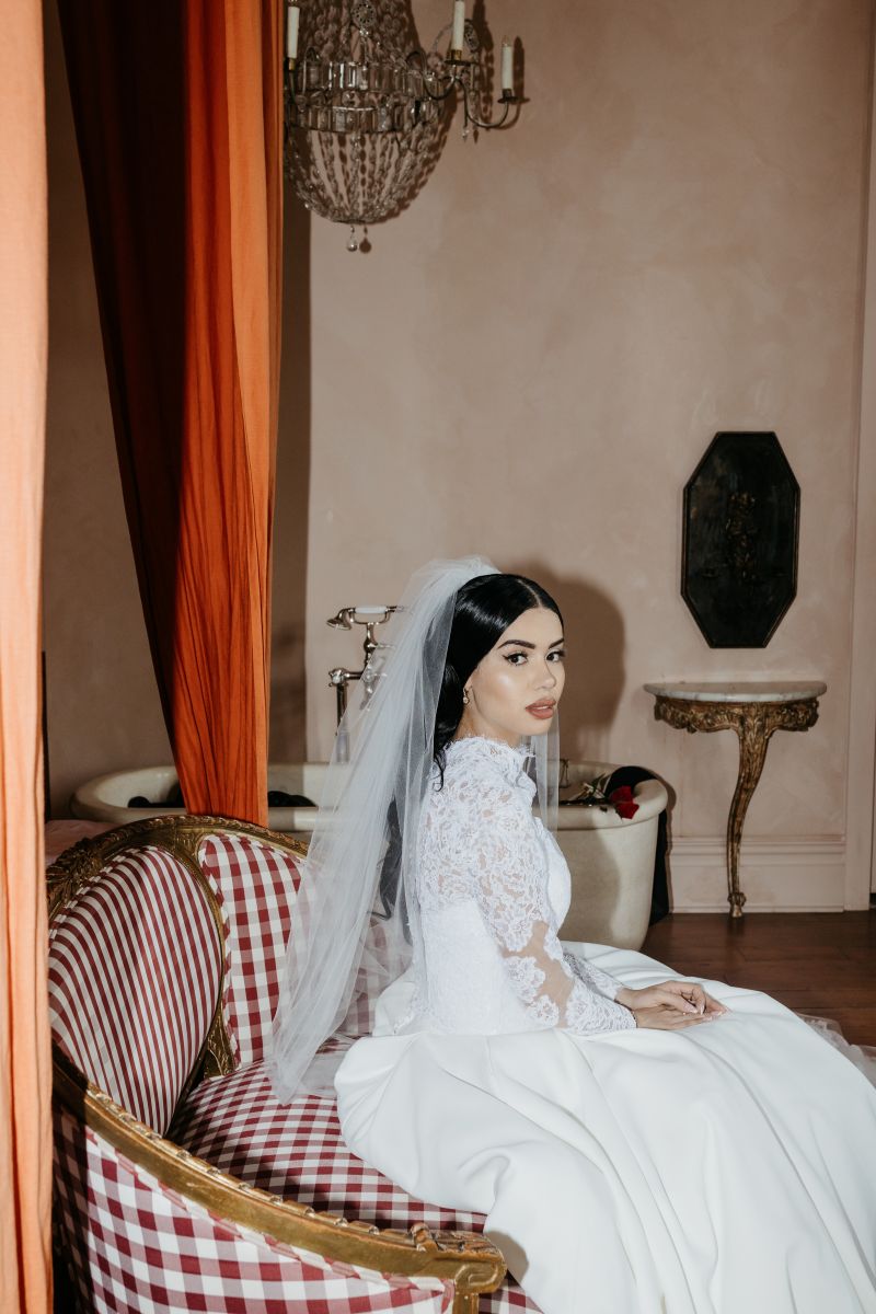 a woman sitting on a plaid red and white couch wearing a white wedding dress and veil 