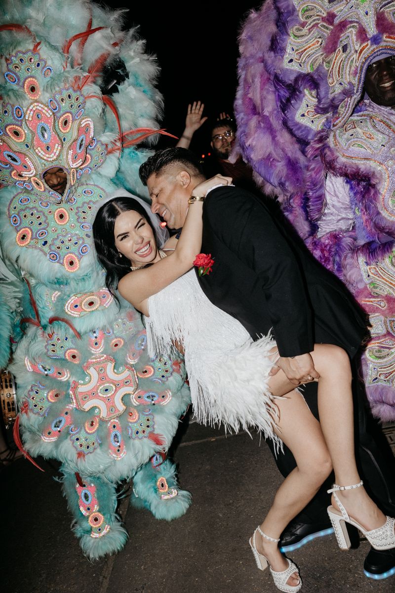 a couple celebrating their marriage with the new orleans mardi gras indians second line the man is dipping his partner backwards