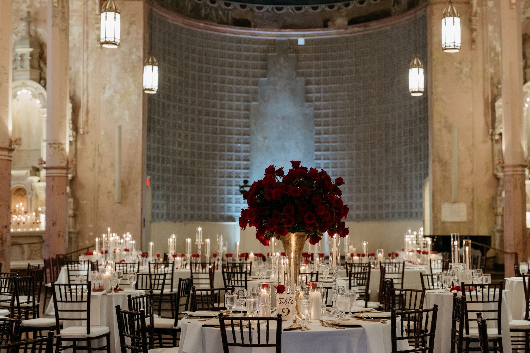 wedding tables elegantly decorated with white table cloths, candles, and red roses inside of hotel peter and paul's chapel 