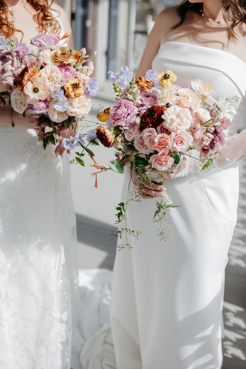 colorful floral bouquets being held by two women wearing white wedding dresses