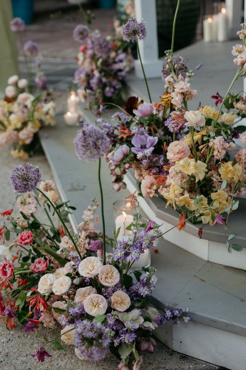 colorful floral arrangements on the steps of derbes mansion surrounded by candles in glass vases