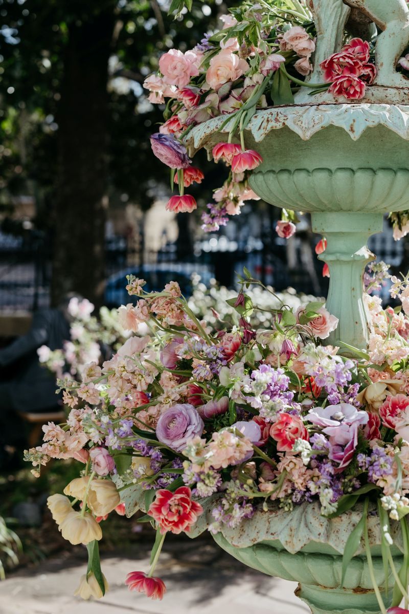 a green fountain decorated with a variety of colorful flowers that include purple, yellow, white, and pink blooms