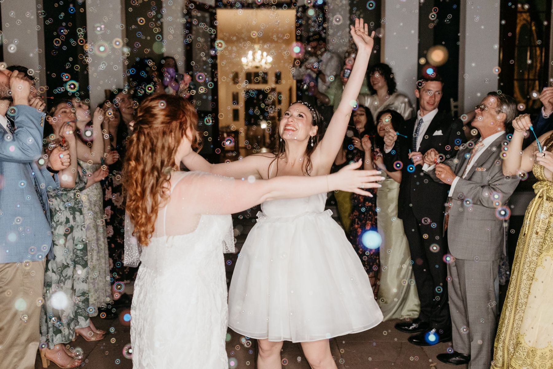 two women dancing at their wedding reception as their guests blow bubbles and watch them