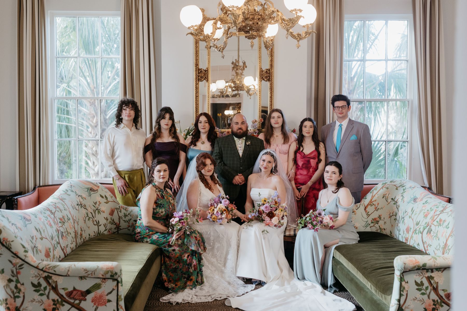 two women sitting side by side with their families standing next to them inside of derbes mansion
