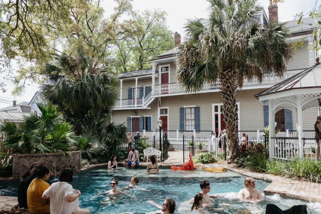 A group of people sitting in a pool in front of a large house 