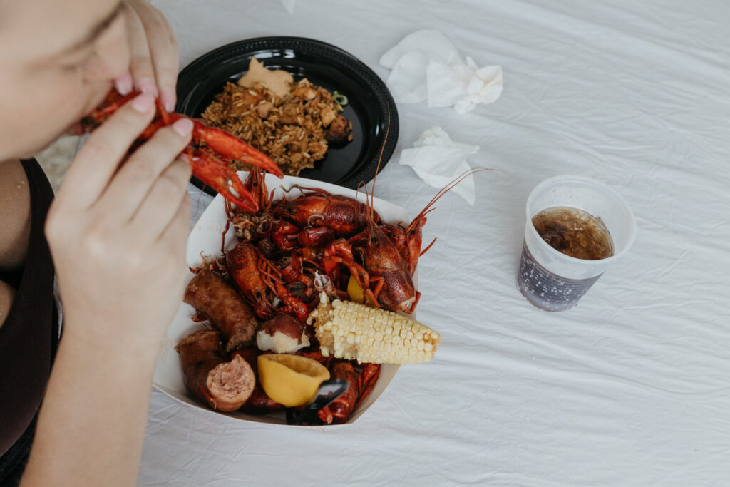 Someone eating crawfish with more on a plate in front of them and a small soda 