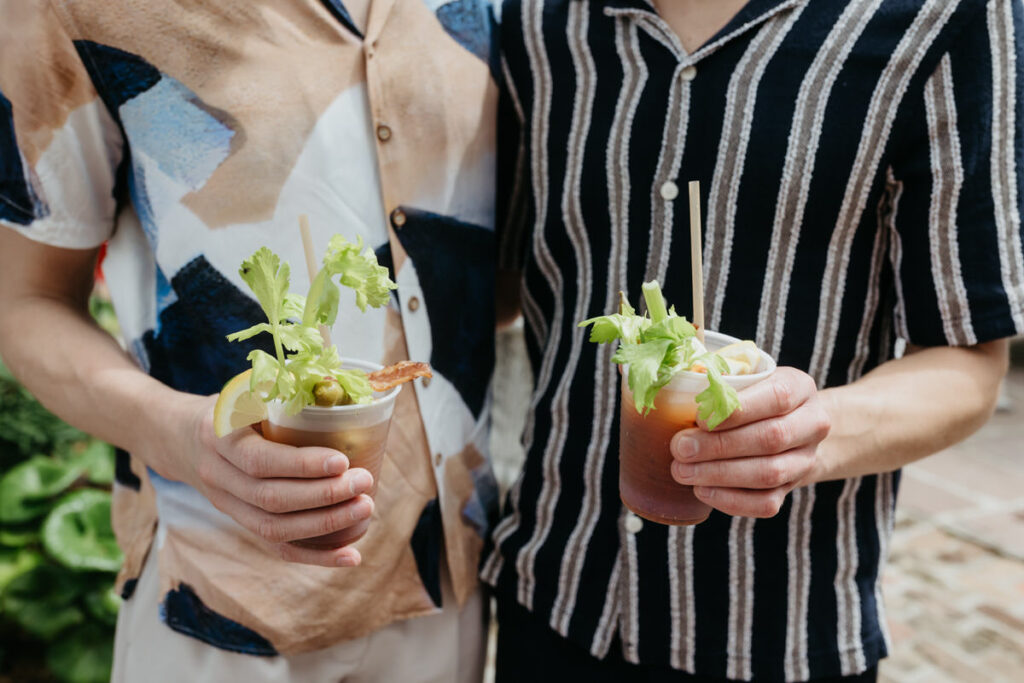 Two people holding plastic cups with Bloody Mary's in them. 