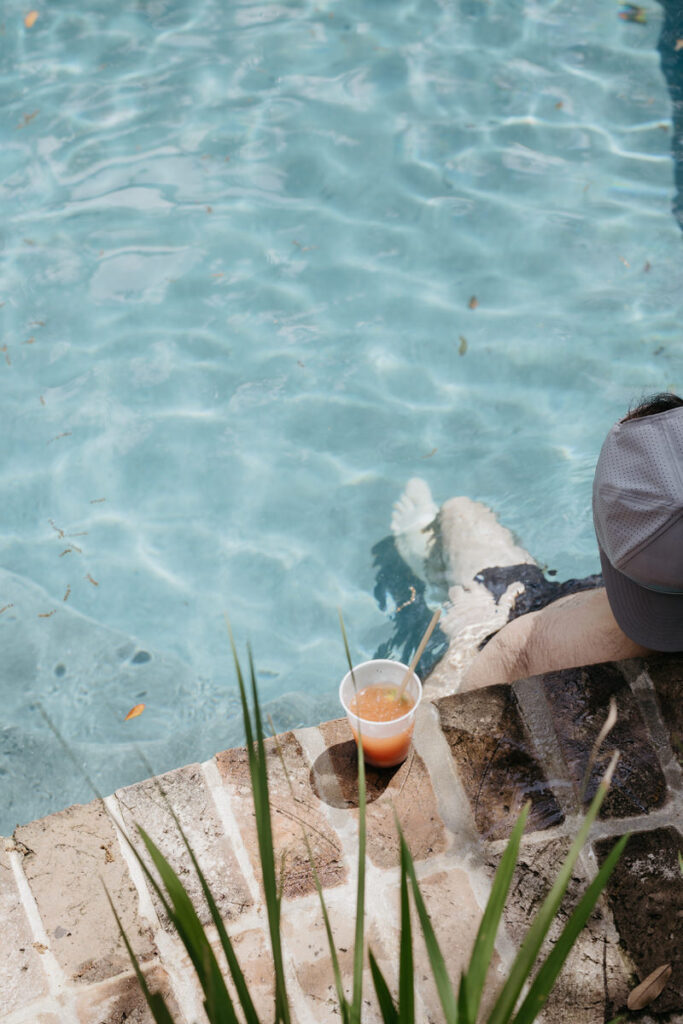 Someone sitting in a pool with a drink on the edge next to them 
