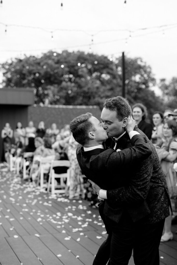 Newlyweds kissing with wedding guests clapping behind them 