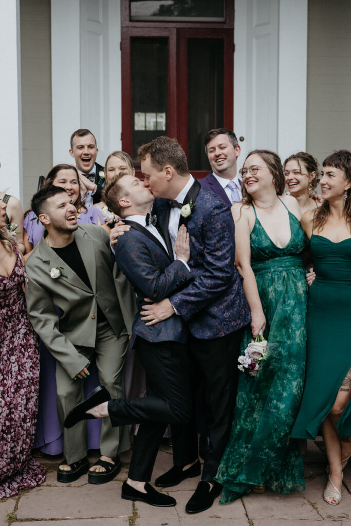 Newlyweds kissing with wedding guests smiling behind them 