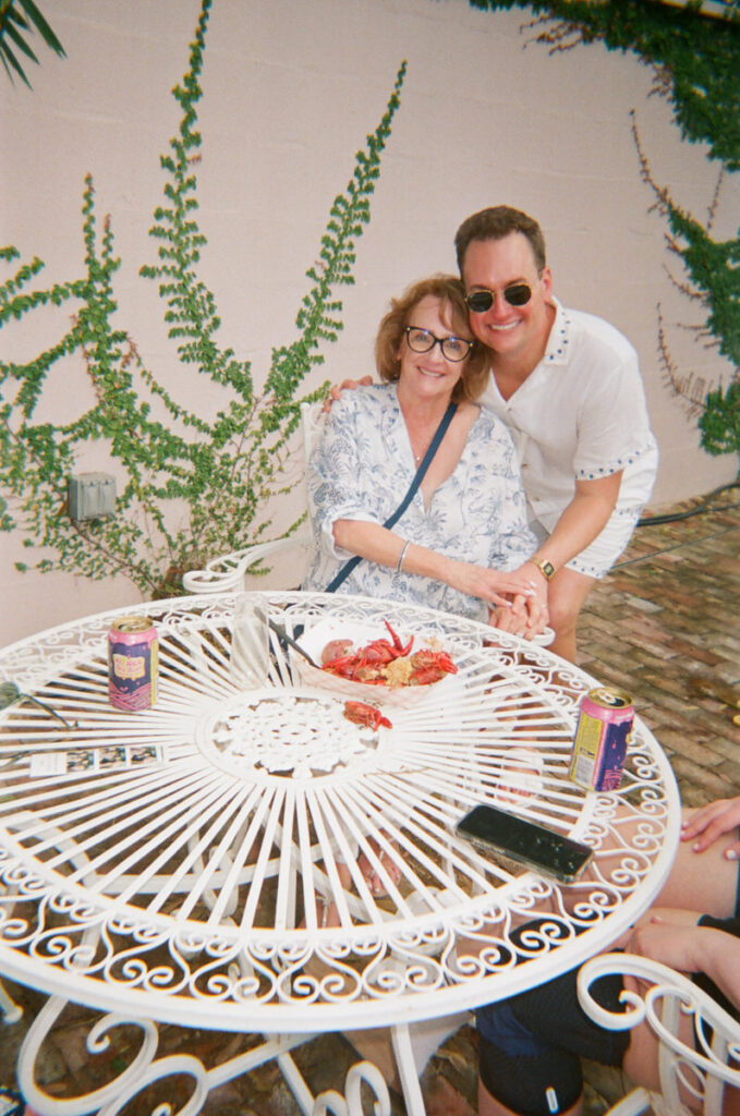 A person leaning down and smiling with their arm around someone else in a chair 