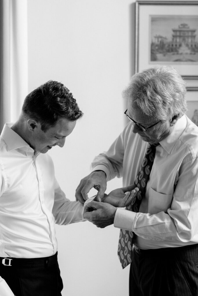An older person helping someone put on cuff links 