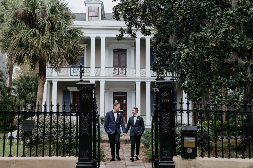 A newlywed couple holding hands and walking out of a mansion 