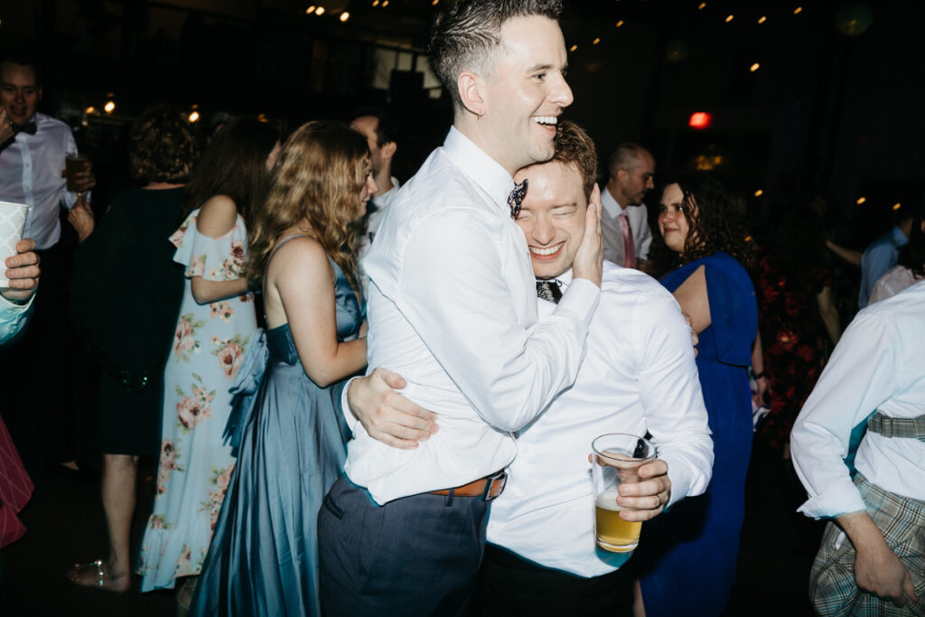 Two people smiling and hugging as one holds a beer 