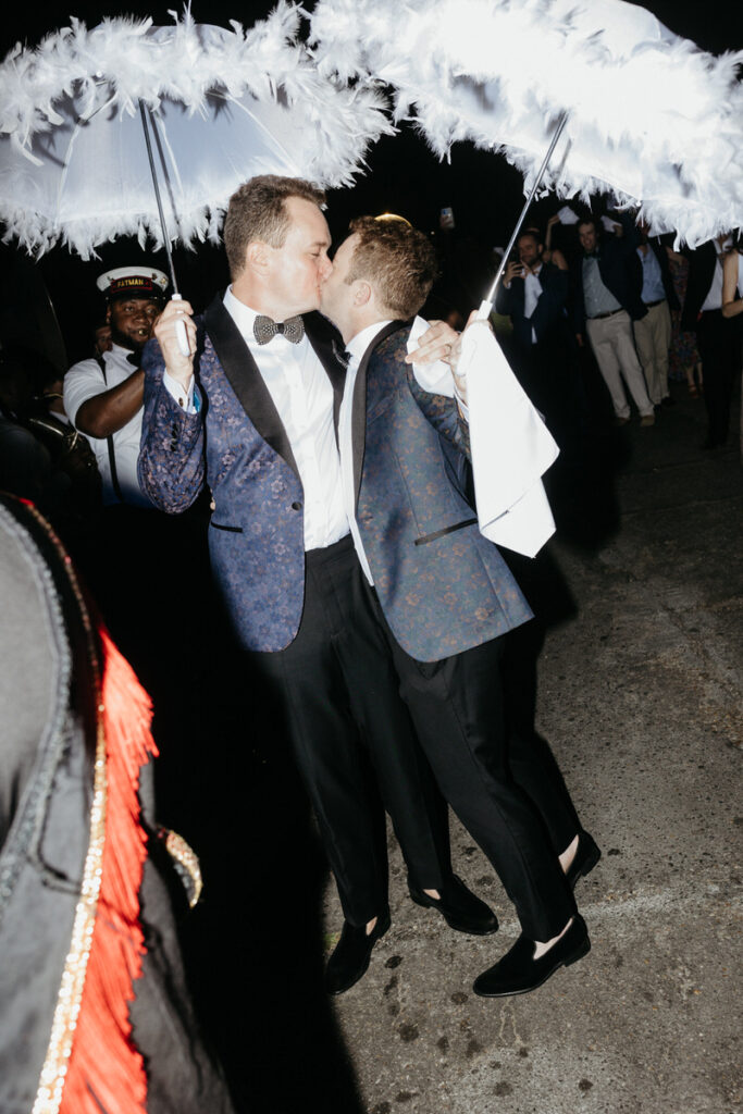 Newlyweds kissing while holding small while umbrellas over their heads 