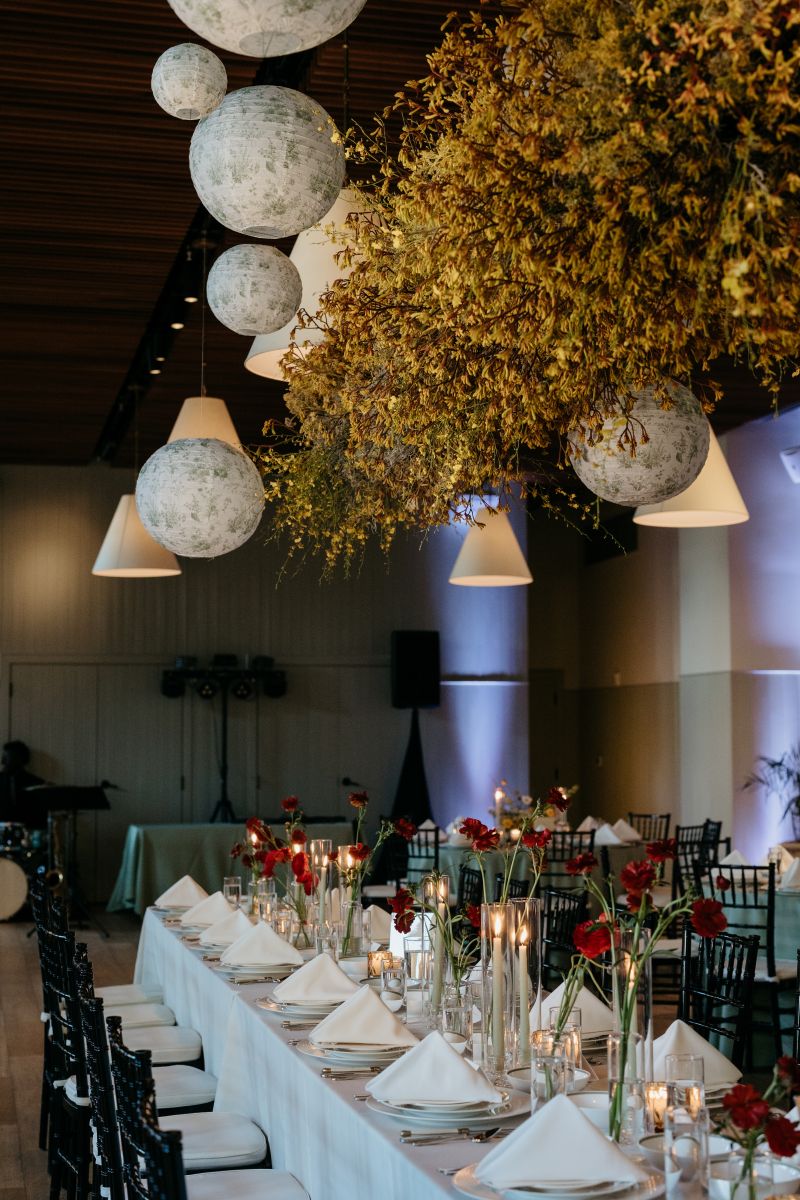 a wedding reception set up at hotel saint vincent with long tables covered in white tablecloths, chairs, a hanging floral installation, and candles