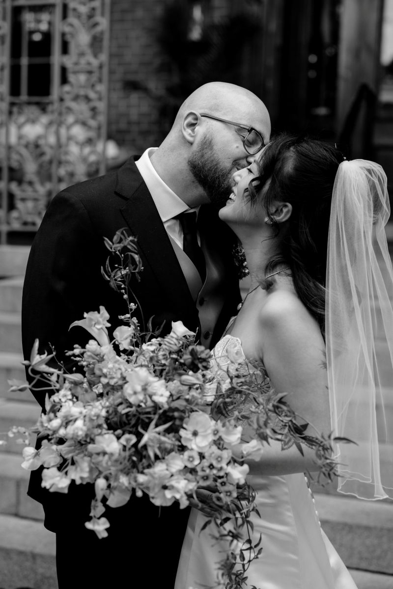 a man kissing his partner on the cheek they are both smiling and the woman is holding a bouquet of flowers