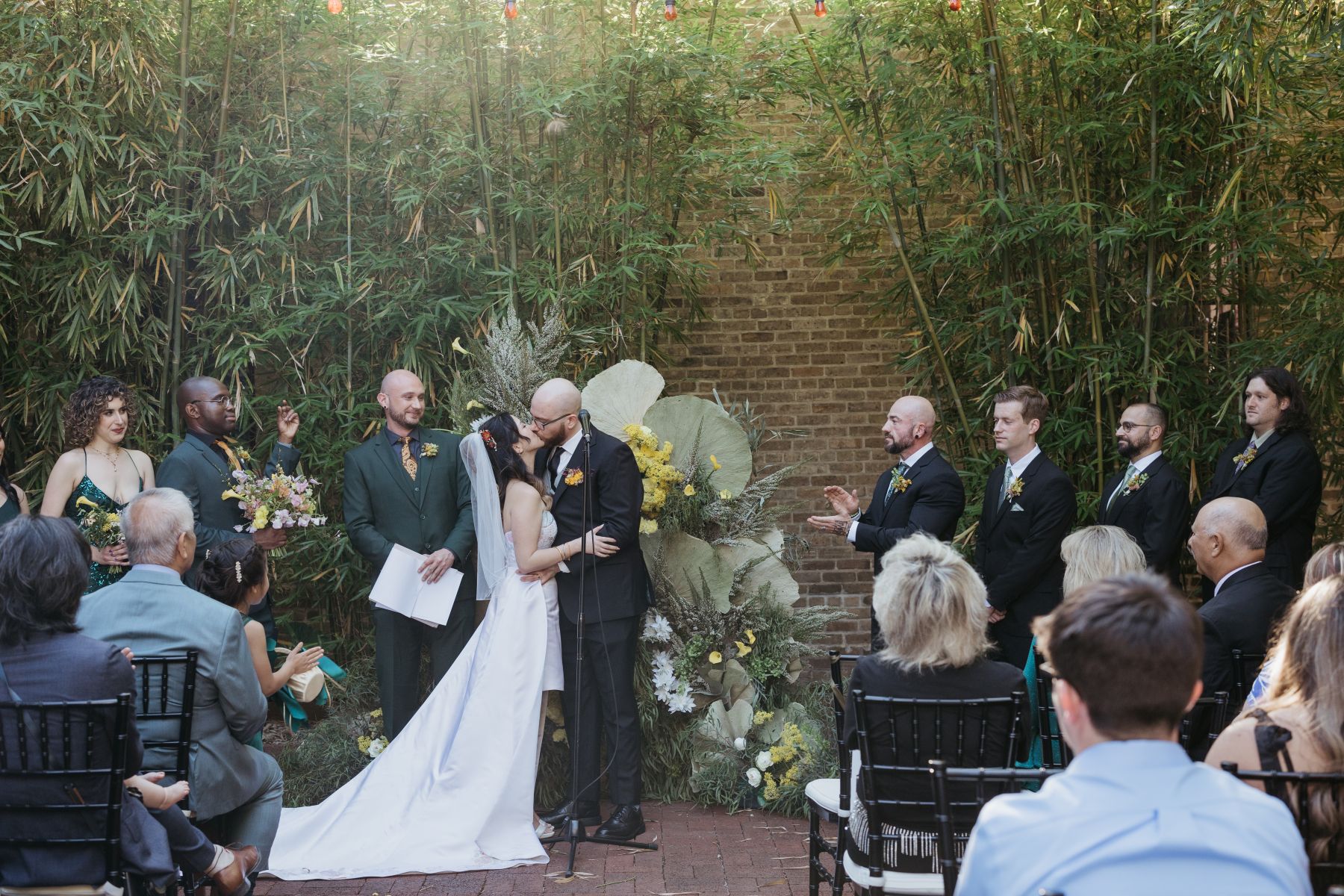 a couple kissing during their wedding reception outdoors at hotel saint vincent in new orleans surrounded by their guests who are cheering for them