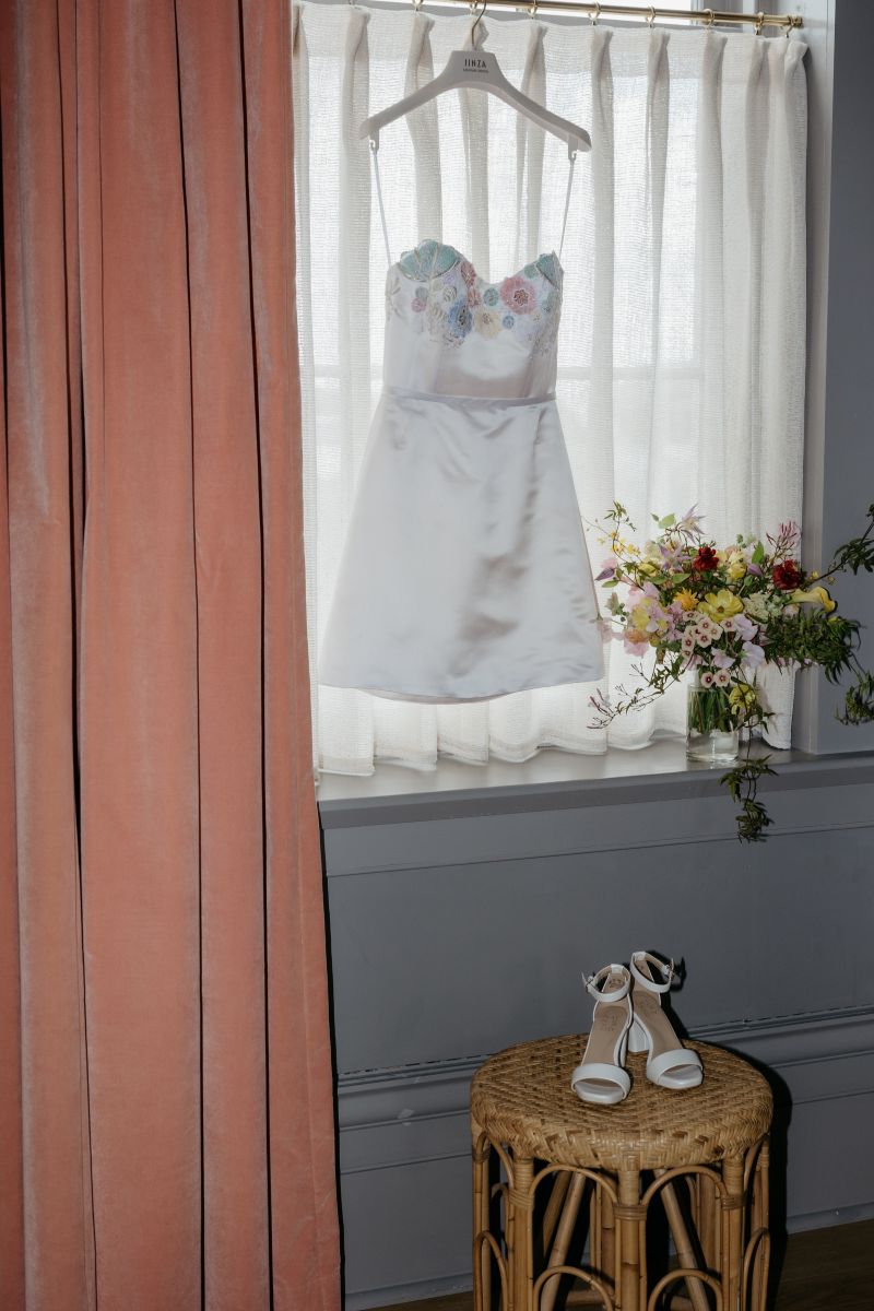 a wedding dress hanging on a curtain rod with white heels perched on top of a side table