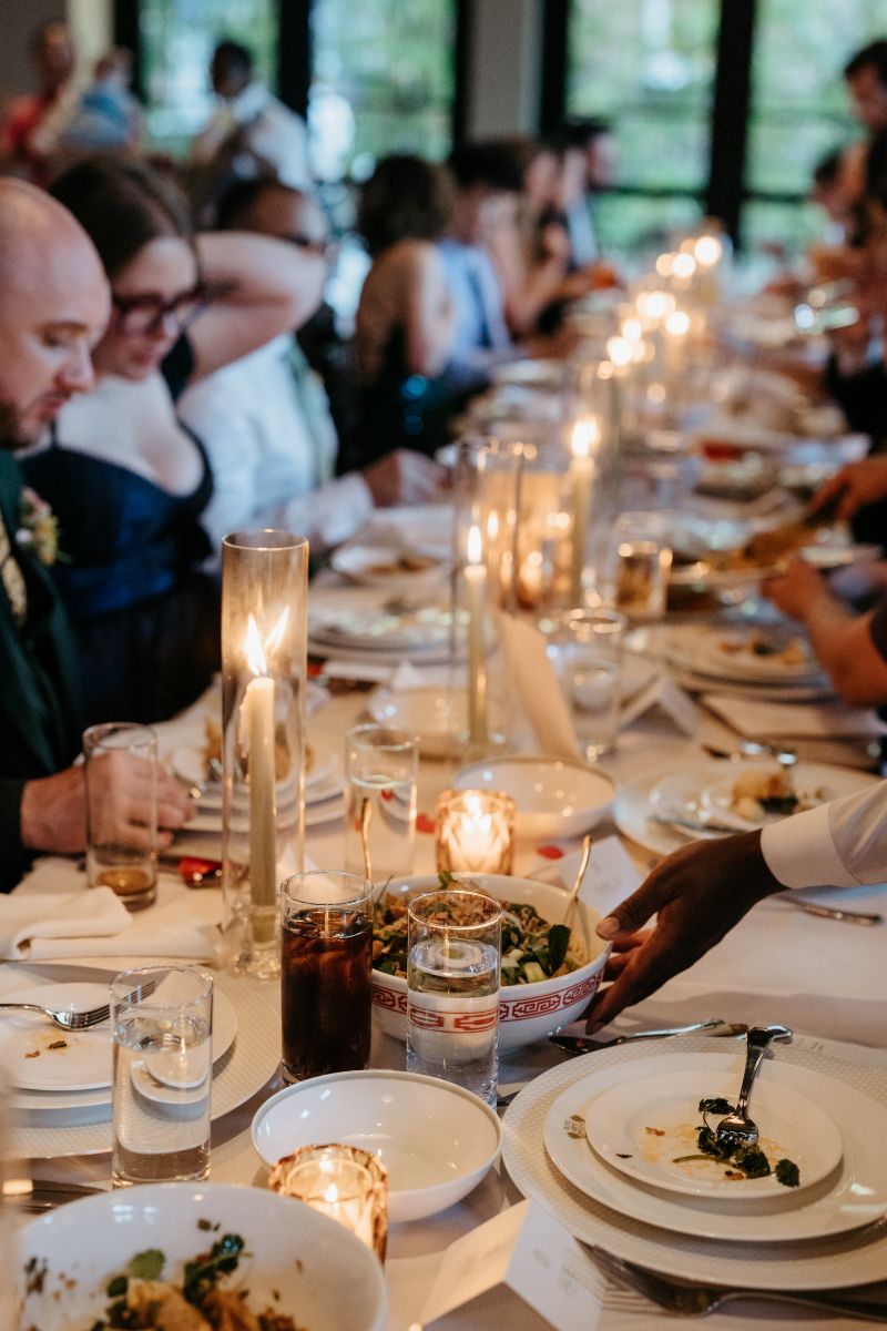 guests at a wedding reception being served dinner the table is covered in candles and a white tablecloth and plates and cutlery