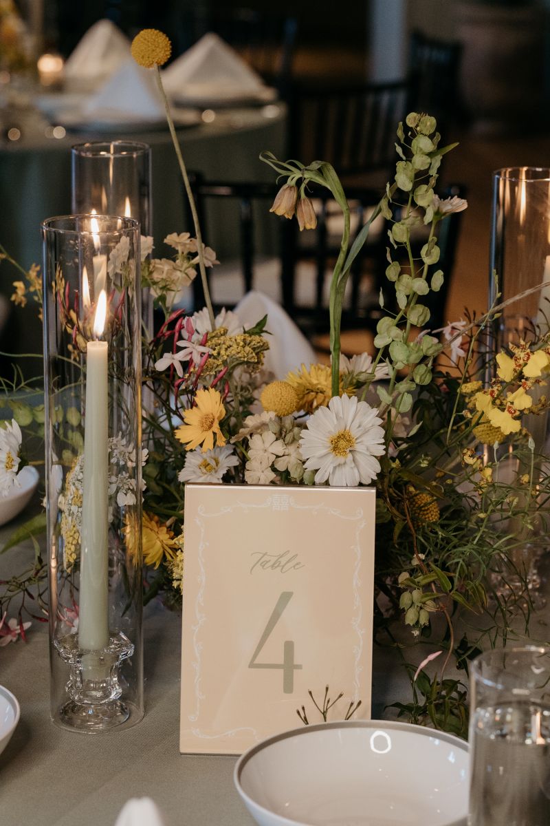 a table at a wedding opulently decorated with colorful flowers, candles in glass vases, and cutlery