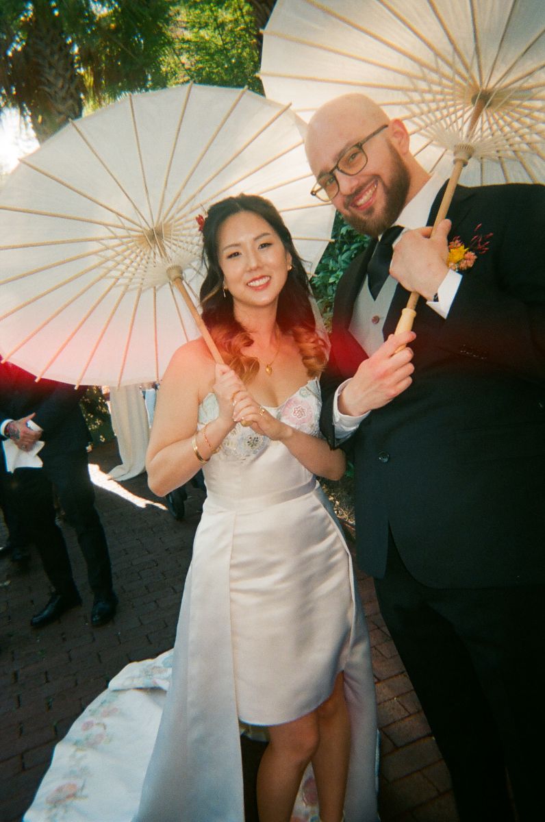 a couple standing together and smiling at their wedding and holding white parasols