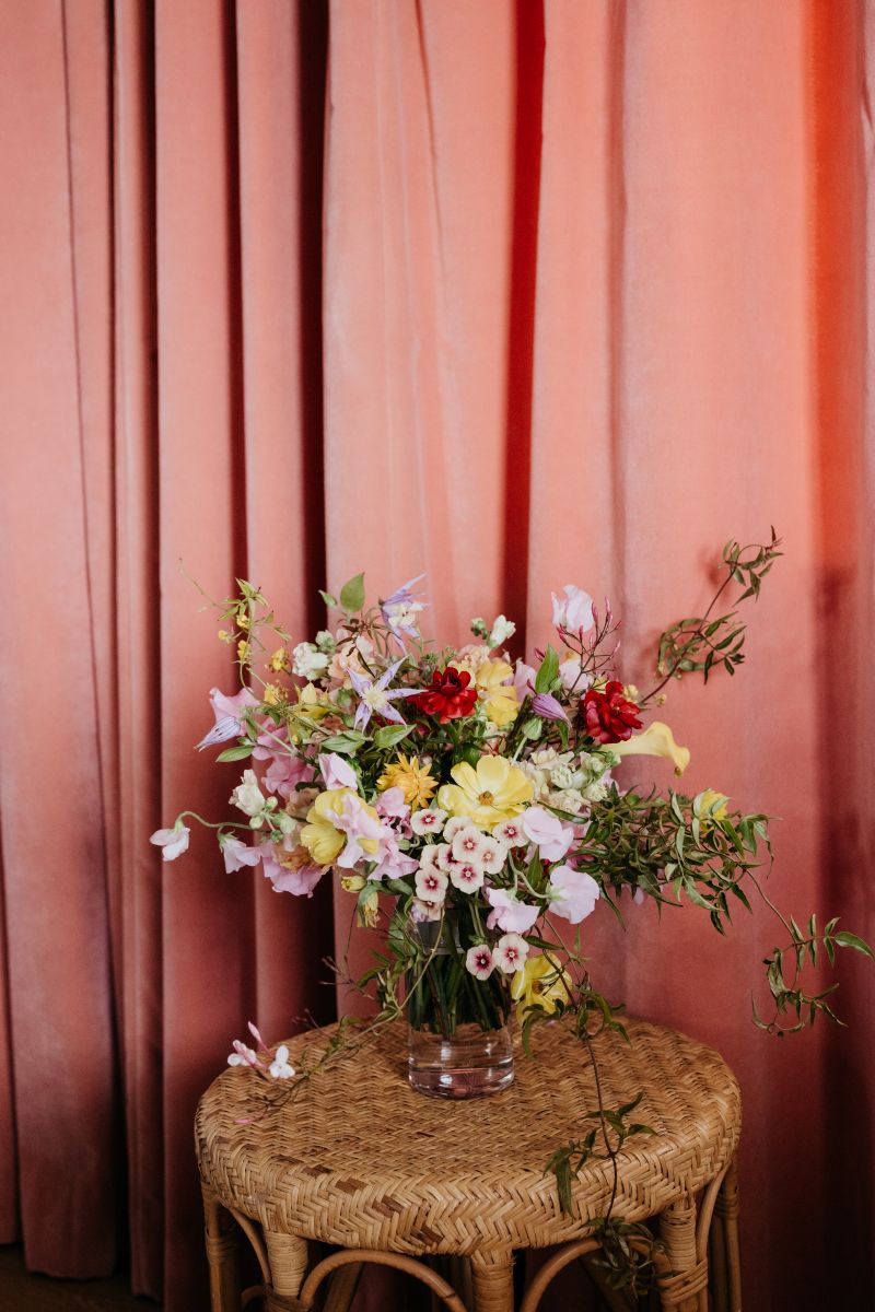 a colorful floral arrangement on top of a table next to a pink curtain