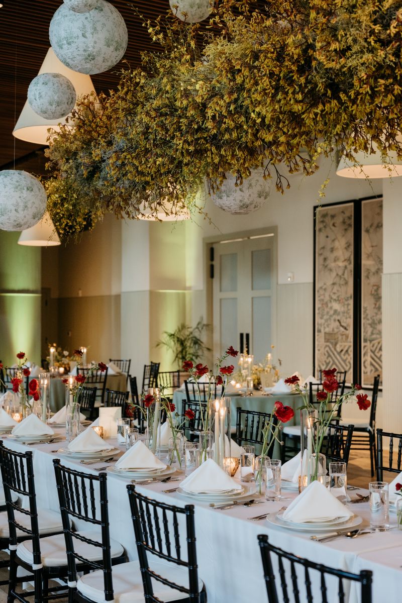 long tables covered in white tablecloths decorated with candles and flowers above the table is a hanging floral installation