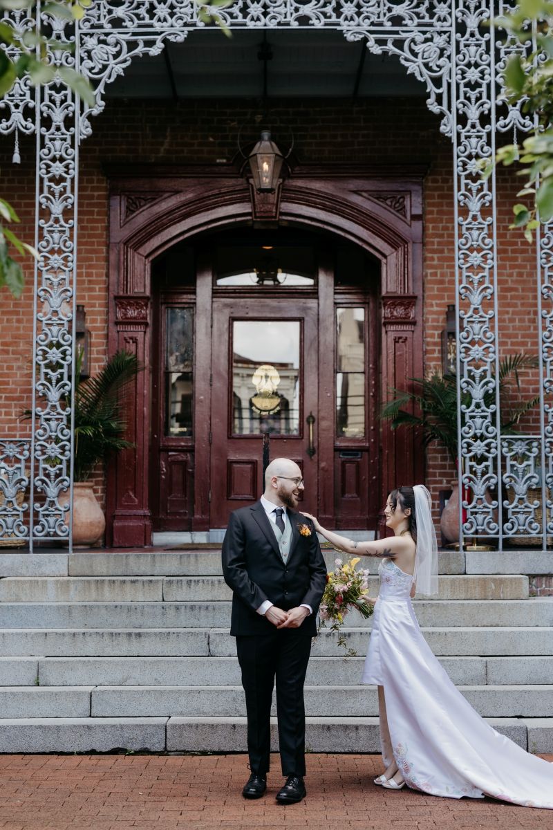 a woman in a white wedding dress and veil walking up to her partner and touching his shoulder they are standing in the entrance of hotel saint vincent